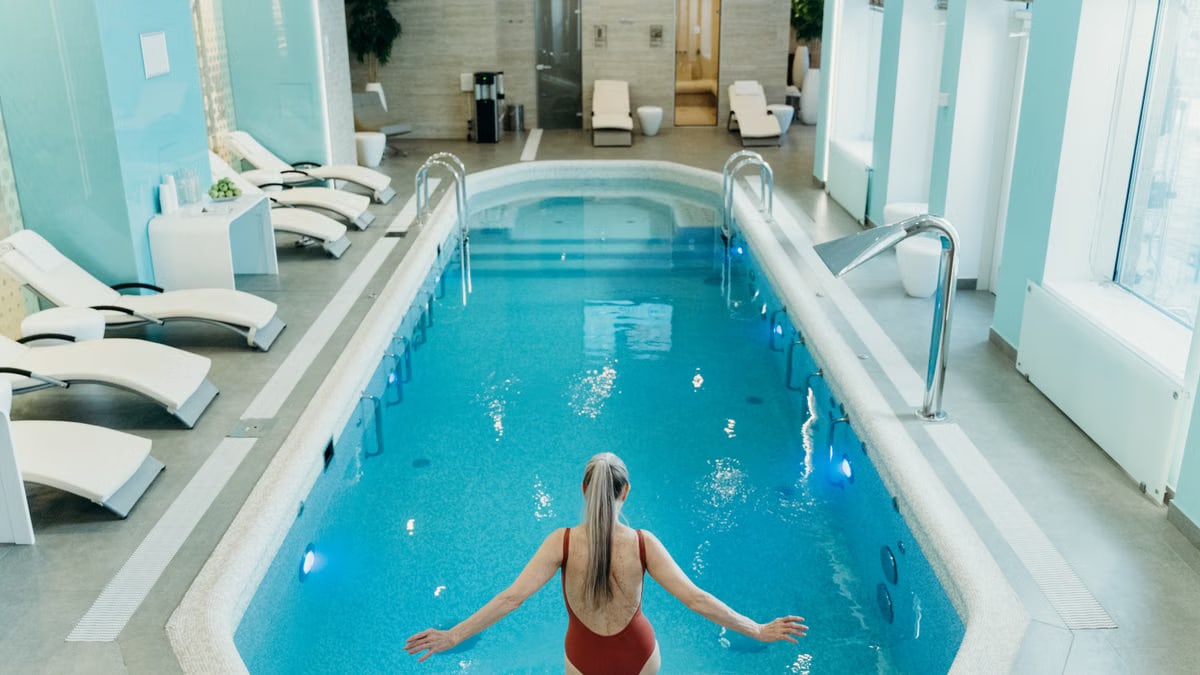 A woman in a red swimsuit prepares to enter an elegant indoor pool at a luxurious spa.